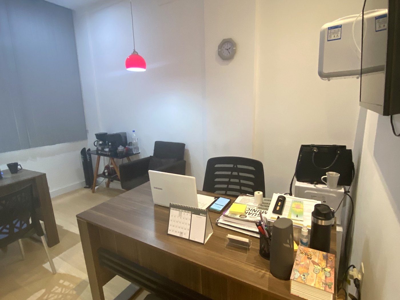 Foto real do escritório vista de outro ângulo, com a mesa de trabalho e as luminárias vermelhas acesas